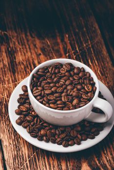 White cup full of roasted coffee beans on saucer