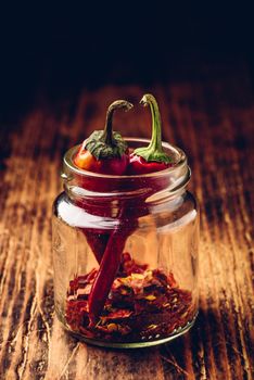 Two dried red chili peppers in jar with ground peppers