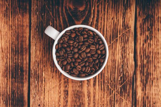 Roasted coffee beans in white cup over rustic wooden surface