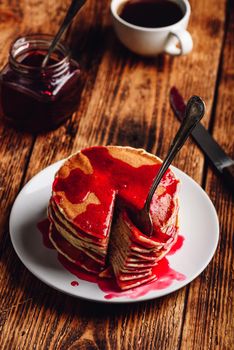 Stack of pancakes with berry jam on white plate over wooden table