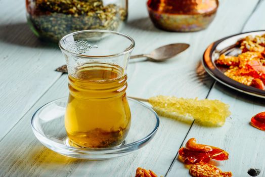 Herbal tea in armudu glass with arabic delights on metal plate over light wooden surface