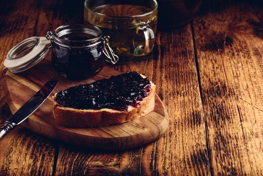 Toast with berry jam on cutting board and cup of green tea