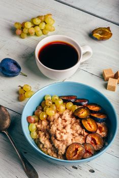 Healthy breakfast concept. Porridge with fresh plum, green grapes and cup of coffee. Ingredients over wooden background.