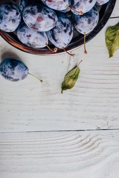 Ripe plums on metal plate over light wooden surface. Copy space