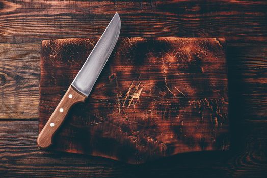 Knife over rustic wooden cutting board. View from above