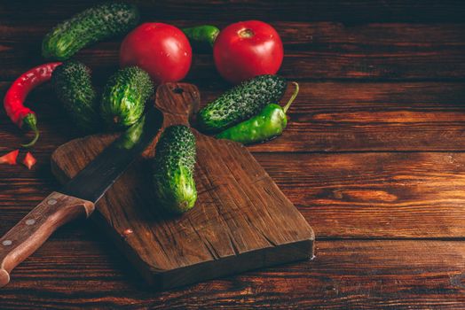 Fresh cucumbers, tomatoes and chili peppers on cutting board for preparing salad.