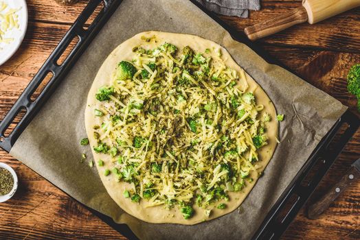 Italian pizza with broccoli, pesto sauce, spices and cheese in a baking tray ready for the oven. View from above