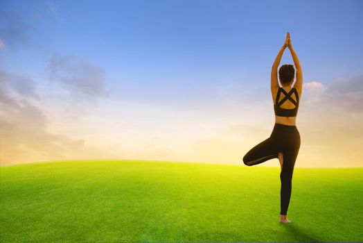 Young girl doing yoga fitness exercise on green field with sunset or sunlight background. Healthy and Yoga Concept.