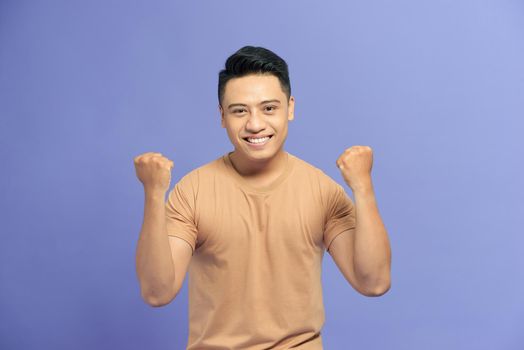 portrait of thrilled man holding fists up, against color background