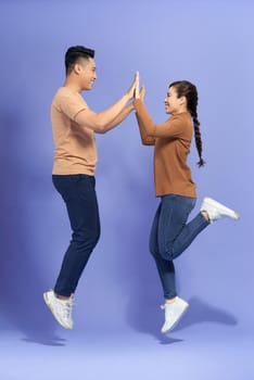 Image of emotional couple friends standing isolated over purple background gives a high five to each other.