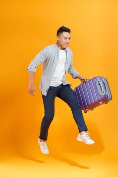 Attractive happy young Asian man tourist with air ticket and passport in his hand jumping isolated on yellow studio background