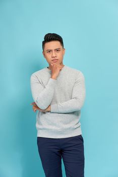 Picture of young thoughtful man dressed standing over blue background