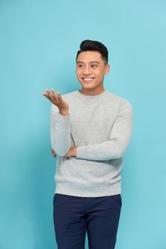 Portrait of happy cheerful young man holding copyspace on palm over blue background
