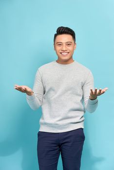 A standing young man raising hands as he saying surprise, isolated on a Blue background.