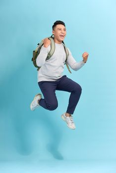 Happy young attractive man jumping and waving his hand, wearing in basic clothes with backpack