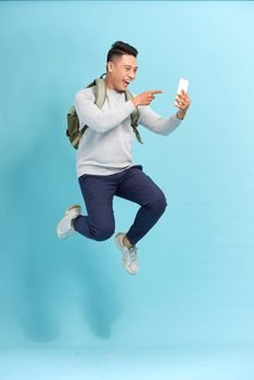 Image of excited young man isolated over blue wall background make selfie by mobile phone jumping.