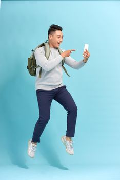 Full length of handsome  young man taking phone while jumping against blue background.