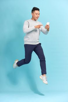 Image of excited young man isolated over blue wall background make selfie by mobile phone jumping.