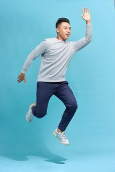 Full-length photo of funny man running or jumping in air isolated over blue background