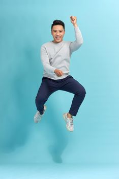 Vertical image of asian man jumping in studio. Isolated blue background