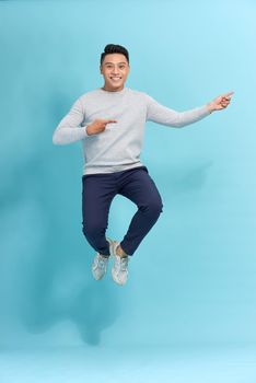 happy young Asian man in casual clothes jumping on blue background