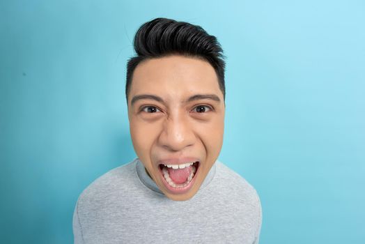 Commanding loudly at the camera. An asian man with gray t-shirt and blue background.