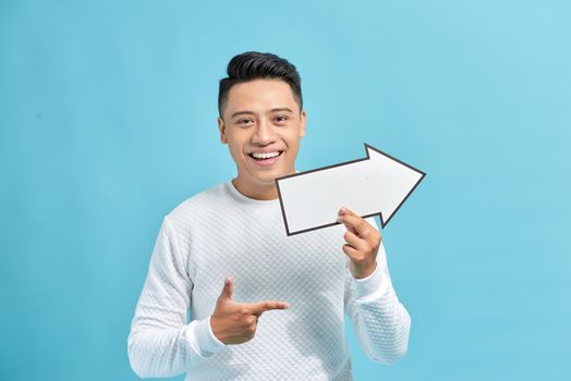 Good looking young man holding a white arrow, isolated on a blue background