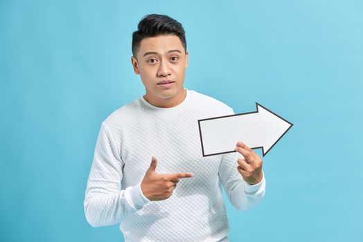 Happy young businessman holding a arrow pointing right and leaning against a wall isolated on blue background