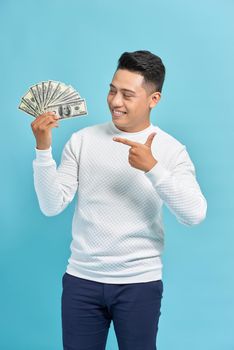 Attractive man wearing a shirt, holding a fan of dollar bills in front of him. blue background.