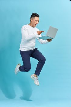 Attractive successful guy jumping in air using laptop home-based job isolated over blue background