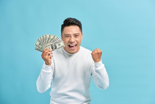 Happy man holding bills of US dollars over blue background