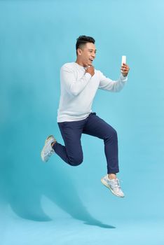 Full length of handsome young man taking phone while jumping against blue studio background