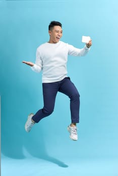 Full length portrait of happy man jumping and screaming while taking selfie on smartphone over blue background