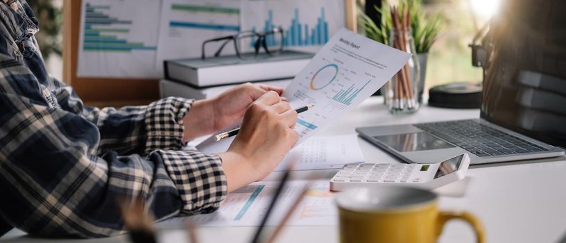 Close up of businessman or accountant hand holding pen working on calculator to calculate business data, accountancy document and laptop computer at office, business concept