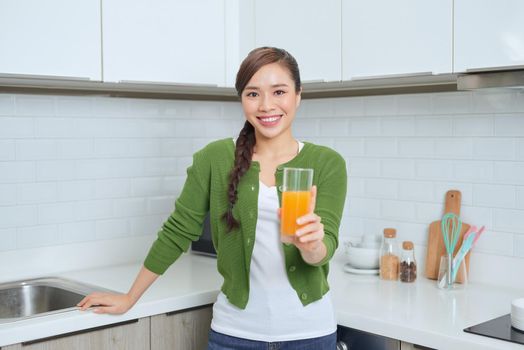Portrait of a smiling young woman drinking orange juice in the kitchen at home
