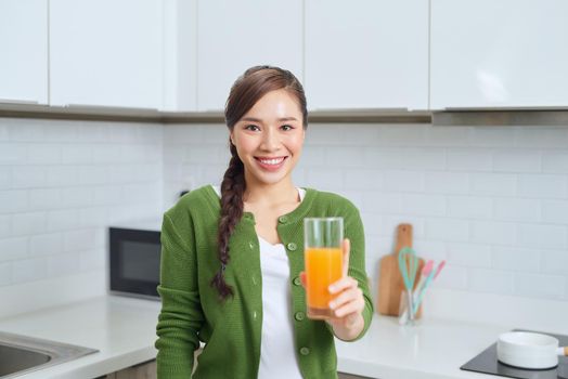 Portrait of a smiling young woman drinking orange juice in the kitchen at home