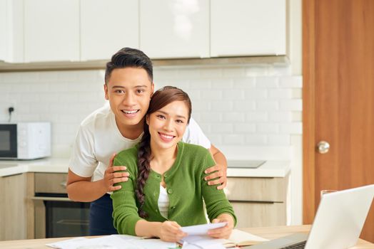 Attractive asian housewife  having happy expression while calculating bills in kitchen