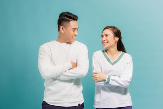 Portrait of a cheerful young couple standing with arms folded and looking at each other isolated over blue background