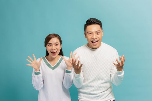 Portrait of optimistic amazed young couple man and woman with arms raised isolated over blue background