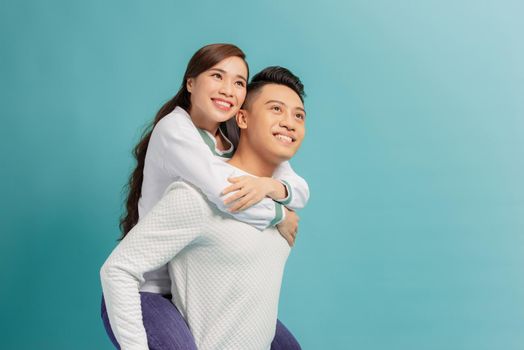 Love forever, fun together. Young handsome boyfriend is piggybacking his cute lover, on blue background