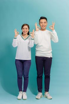 Image of cheerful multinational man and woman smiling and gesturing ok sign isolated over blue background