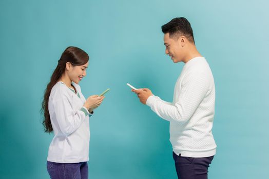 Face-to-face conversation. Excited man and woman talking holding smartphones looking at each other standing over blue background.