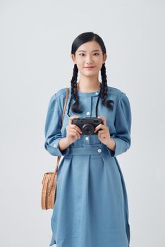Smiling good looking Asian woman with long pigtail holds retro camera, takes pictures during her awesome trip