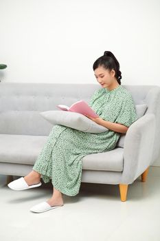 Young woman reading humorous novel while sitting on sofa