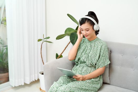 Smiling beautiful asian listening music while using her tablet in the living room