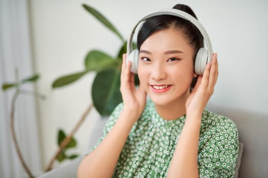 Woman listening music in headphones while sitting on sofa in room