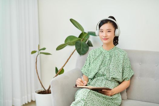 Woman listening to music and writing diary on sofa at home