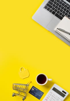 Online shopping concept. Top view of credit card purchase design concept with note, calculator and computer isolated on office yellow table background.