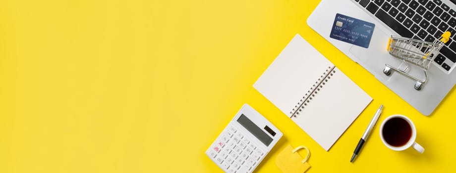 Online shopping concept. Top view of credit card purchase design concept with note, calculator and computer isolated on office yellow table background.