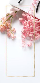 Pink spring flowers, pink gift streamers in white gift bag on white background. Beautiful spring card for Birthday, Woman, Valentines, Mothers Day in pastel colours. Vertical flat lay. Copy space